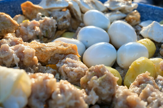 Steaming Indonesian street food dish containing siomay dumplings, tofu, potatoes, and peeled quail eggs. Suited for Southeast Asian street food culture, traditional steaming methods, local culinary