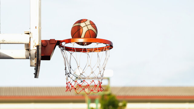 Basketball dropping through hoop on outdoor court with clear sky and soft background