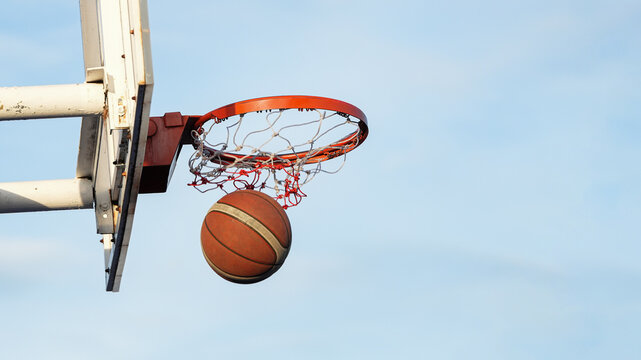 Basketball hoop and ball captured during scoring moment on sunny outdoor court