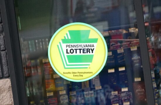 Pennsburg, Pennsylvania, U.S.A - May 12, 2026 - Pennsylvania Lottery logo sticker on glass door with products visible inside store.