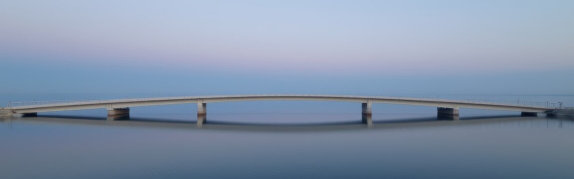 Modern bridge spanning calm water under clear sky at dusk