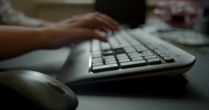 Close up view of hands typing on a black computer keyboard and operating a mouse on a dark desk surface