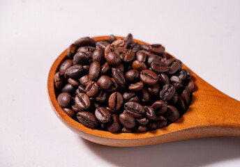 Fototapeta premium Close-up of roasted coffee beans in a wooden spoon on a wooden table with dark background, showcasing rich aroma and premium coffee concept.