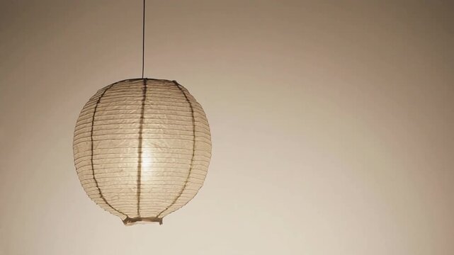 A round paper lantern hangs from a thin cord against a plain beige wall.