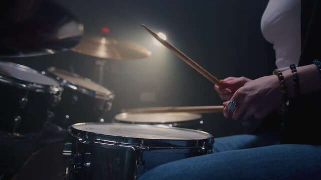 Young female drummer passionately playing a drum kit in a professional rehearsal studio, energetically striking cymbals and drums with drumsticks. Hair flying. Rock Feminist style. Woman power.
