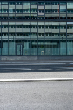 Beyond the road, a glass building facade compresses into view, with windows and reflection aligned over the street sidewalk in urban architecture