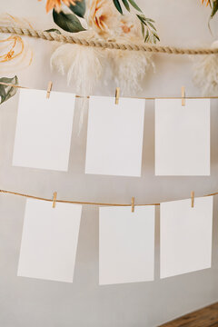 Boho wedding seating chart mockup with six vertical cards hanging on rope. Blank table plan template with wooden clothespins, pampas grass and wall decoration backdrop.
