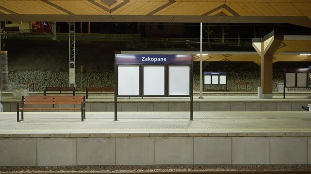 Empty Zakopane railway station platform at night in Poland features station sign and regional wooden design elements. Quiet transit hub for tourists visiting Tatra mountains resort.