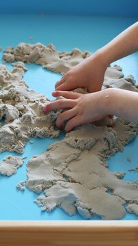 Children activity with kinetic sand for motor and sensory development. Toddler play therapy in wooden sandbox at home.