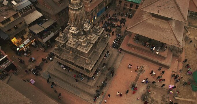 An aerial close-up reveals the intricate stone spire of a Newari temple rising above Patan Durbar Square as tourists and locals gather around its tiered base.