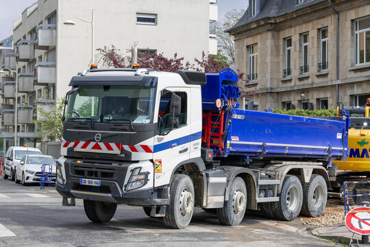 Nancy, France - April 25th 2022 : View on a white and blue 8X4 dump truck Volvo FMX 500 parked on a street for earthworks on a construction site with buildings in the background.