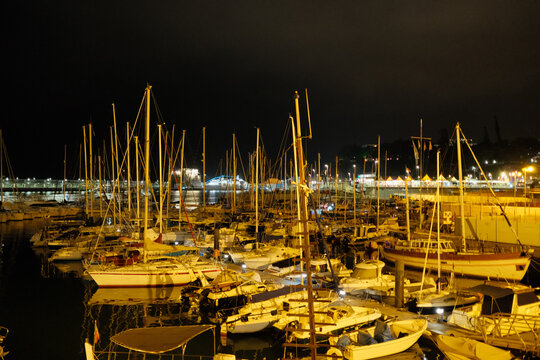 Calm marina at night with anchored vessels and glowing cityscape