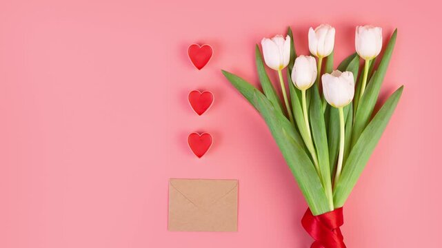 White tulips and red hearts arranged on a pink background for a romantic occasion