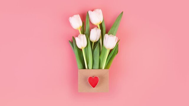 White tulips in a kraft paper envelope with a red heart on a pink background