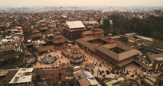 Wide aerial view over the temples and palace courtyards of Patan Durbar Square, with the dense Kathmandu Valley sprawling to the hazy horizon.