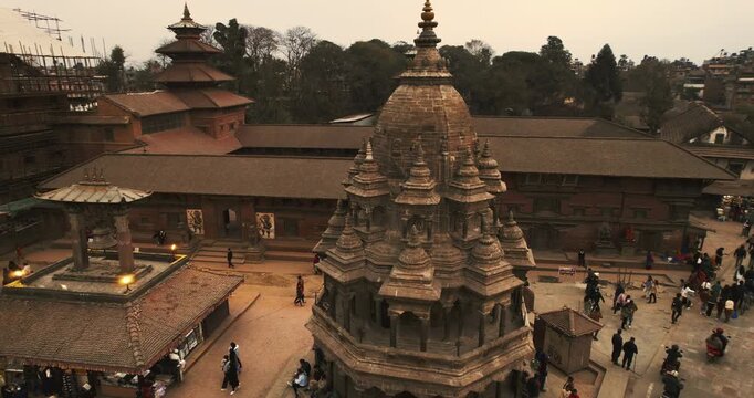 Aerial view of an ornate stone shikhara temple in Patan Durbar Square, surrounded by pagoda roofs and crowds in the historic Kathmandu Valley, Nepal.