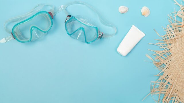 Summer vacation essentials: snorkeling gear, sunscreen, and seashells on blue background