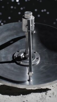 Vertical video: Activating actuator, metal dish pivoting on lunar surface, aiming at blue planet