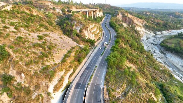 Aerial tracking shot of vehicles on a scenic mountain highway in India. Smooth aerial tracking shot following the flow of traffic along a vital national highway
