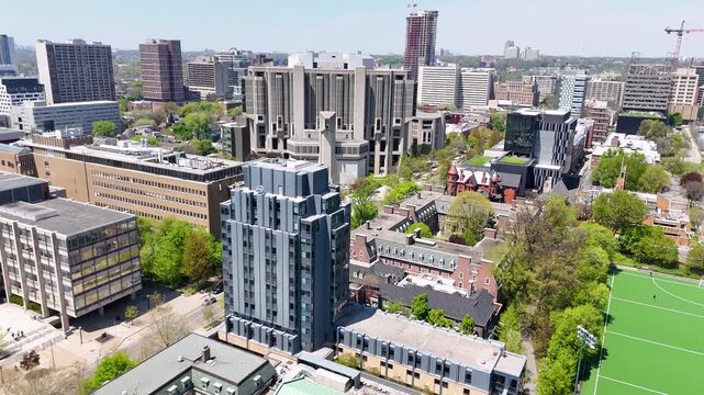 Aerial view flying forward over surrounding university buildings and green trees toward the distinct brutalist architecture of Robarts Library