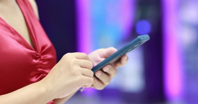 Woman in red dress using smartphone, typing and scrolling on mobile screen with neon background. Technology, communication, and social media concepts, close-up
