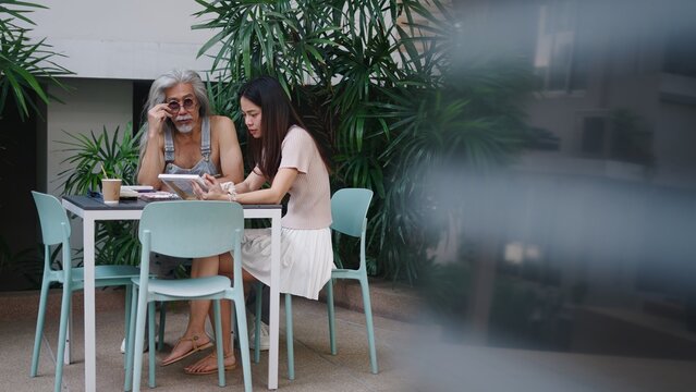 Intergenerational duo discussing on tablet, older man learning from young woman
