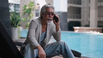 Fototapeta premium Senior asian man making phone call by pool embodying modern lifestyle