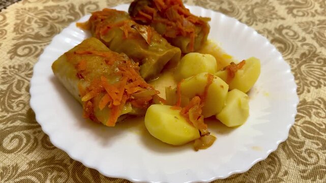 Cabbage rolls meat potatoes on plate, rustic homestyle serving on white plate over patterned tablecloth, warm tomato sauce glazing