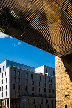 A wood canopy frames sky, facade, and a distant apartment building in Lyon&rsquo;s La Confluence neighborhood, shaping a layered urban exterior view