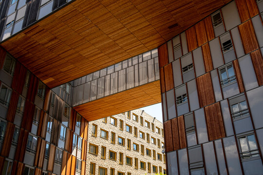 Wood soffits frame a courtyard between apartments in Lyon&rsquo;s La Confluence neighborhood, layering facade planes into a warm urban exterior