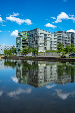 Apartments in Lyon&rsquo;s La Confluence neighborhood reflect across still water, where sky and clouds double the modern building in a bright urban exterior