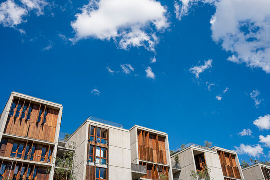 Wood balconies rise above apartment facades in Lyon&rsquo;s La Confluence neighborhood, opening the urban exterior toward a vivid sky and clouds