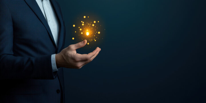  man in a suit holds a glowing, magical orb of light and particles against a dark background.