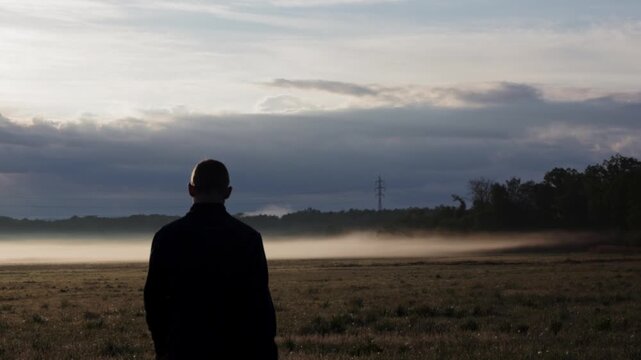 Man silhouette walking on meadow with fog. Lifestyle, rear view