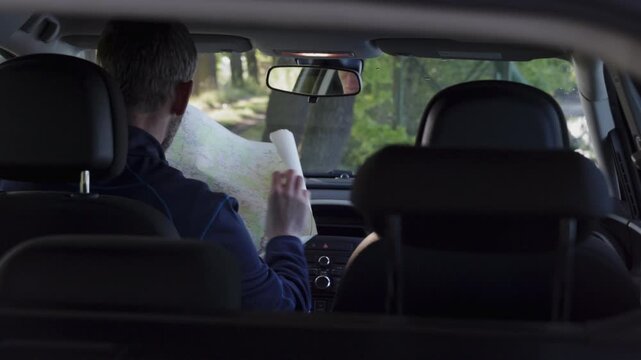 Middle age man sitting in car and searching in paper map to find way. Travel, adventure lifestyle concept