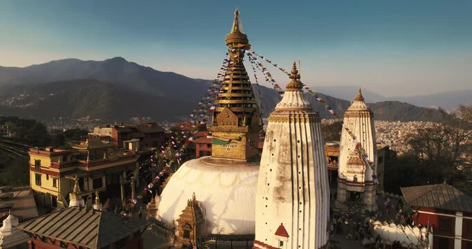 Aerial drone shot of the iconic Swayambhunath Stupa in Kathmandu, featuring its golden spire, watchful Buddha eyes, and colorful prayer flags streaming against the Himalayan foothills.