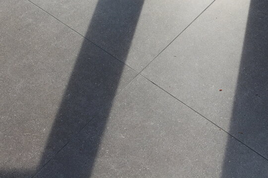 Geometric shadows cast across textured gray concrete tiles on a sunny day
