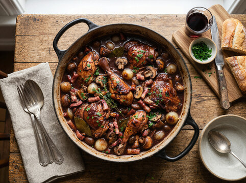 Traditional french coq au vin chicken stew in a pot on a rustic wooden table