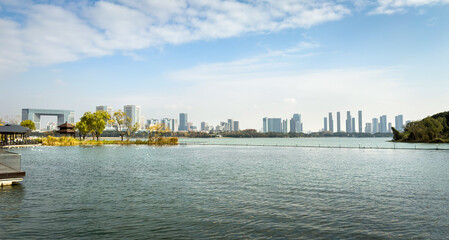 Naklejka premium Serene Waterfront View with Urban Skyline and Lush Greenery