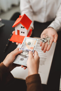 Client hands over cash in exchange for house keys and real estate model, representing investment in property, mortgage settlement, and home ownership concept