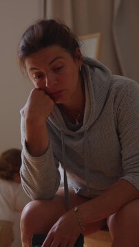 Mentally drained mother sitting quietly while young child rides scooter nearby indoors capturing emotional overload parental fatigue and realistic modern family dynamics