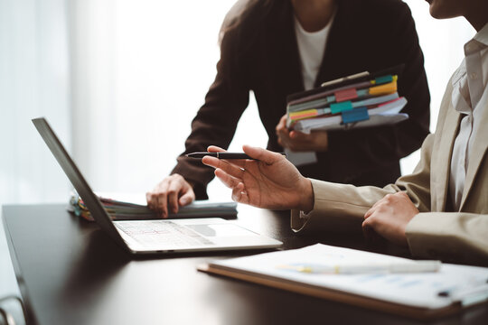 Businesswomen collaborating on a laptop, discussing reports and strategy in a modern office, showing teamwork, mentorship, and financial administration in a corporate setting