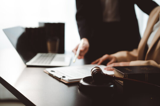 Legal professionals analyzing a contract document with a pen, laptop, gavel, and law book on a dark desk, representing legal consultations, agreements, and courtroom proceedings
