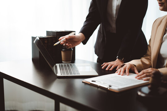 Legal professionals collaborating, reviewing important contract documents on a laptop and clipboard, providing legal advice and consultation in a law firm setting