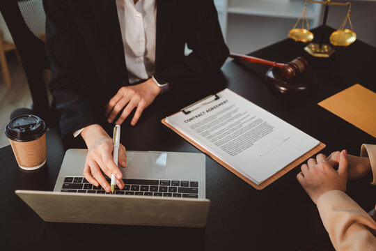 Lawyer meeting with client in office, discussing legal contract agreement while using a laptop with justice scales and gavel on the desk, providing consultation