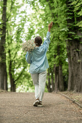 Fototapeta premium Flowers Daisies Woman Walking, Park: Woman with daisies strolls in park, raising arm on sunny day in natural setting.
