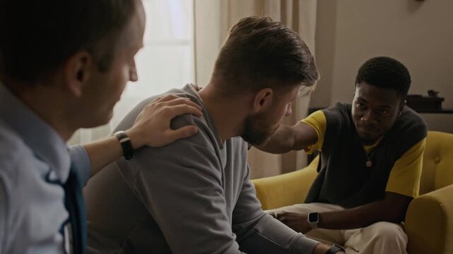 Medium shot of Caucasian and African American men patting friends shoulder, trying to support while he drinking bourbon