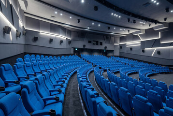 Naklejka premium Empty modern cinema auditorium featuring curved rows of bright blue seats and acoustic walls