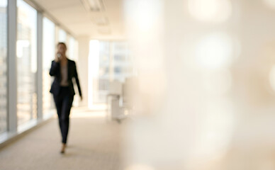 Fototapeta premium A blurred image of a businesswoman walking in a modern office corridor while speaking on her phone, emphasizing a professional work environment.