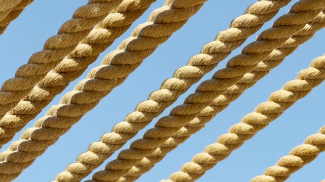A close-up view of thick, rustic ropes stretching diagonally against a bright blue sky. Their coarse, twisted fibers provide a warm and calming texture that evokes a breezy coastal charm.